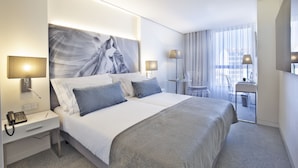 Een moderne hotelkamer met een groot bed, bedlampjes, een bureau en uitzicht op de stad door grote ramen.