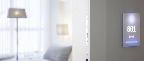 Une chambre d’hôtel moderne, équipée d’un lit, d’une lampe et d’un panneau de commande fixé au mur, affichant le numéro 801.
