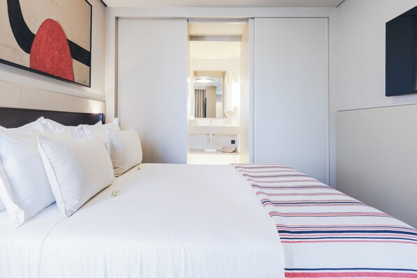 Habitación de hotel con cama, almohadas, una manta a rayas, un espejo y un cuadro en la pared.