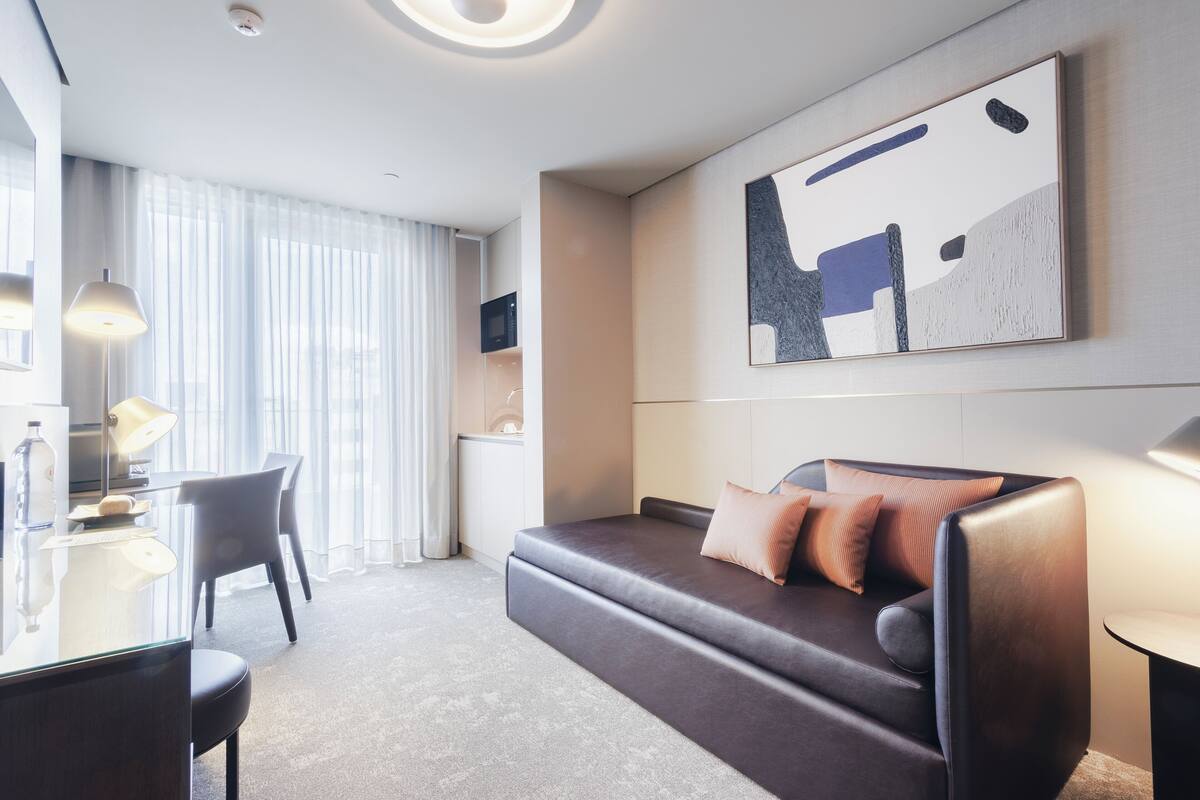 Een moderne hotelkamer met een sofa, een bureau, een lamp en een groot abstract schilderij aan de muur.