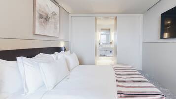 A hotel room with a bed, a flat-screen TV, a framed artwork, and a bathroom visible through an open door.