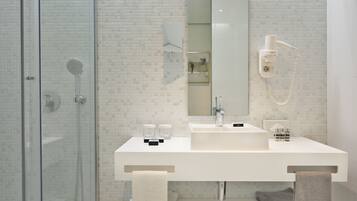 Une salle de bain moderne avec une douche à parois de verre, un lavabo blanc avec un miroir et un sèche-cheveux fixé au mur.