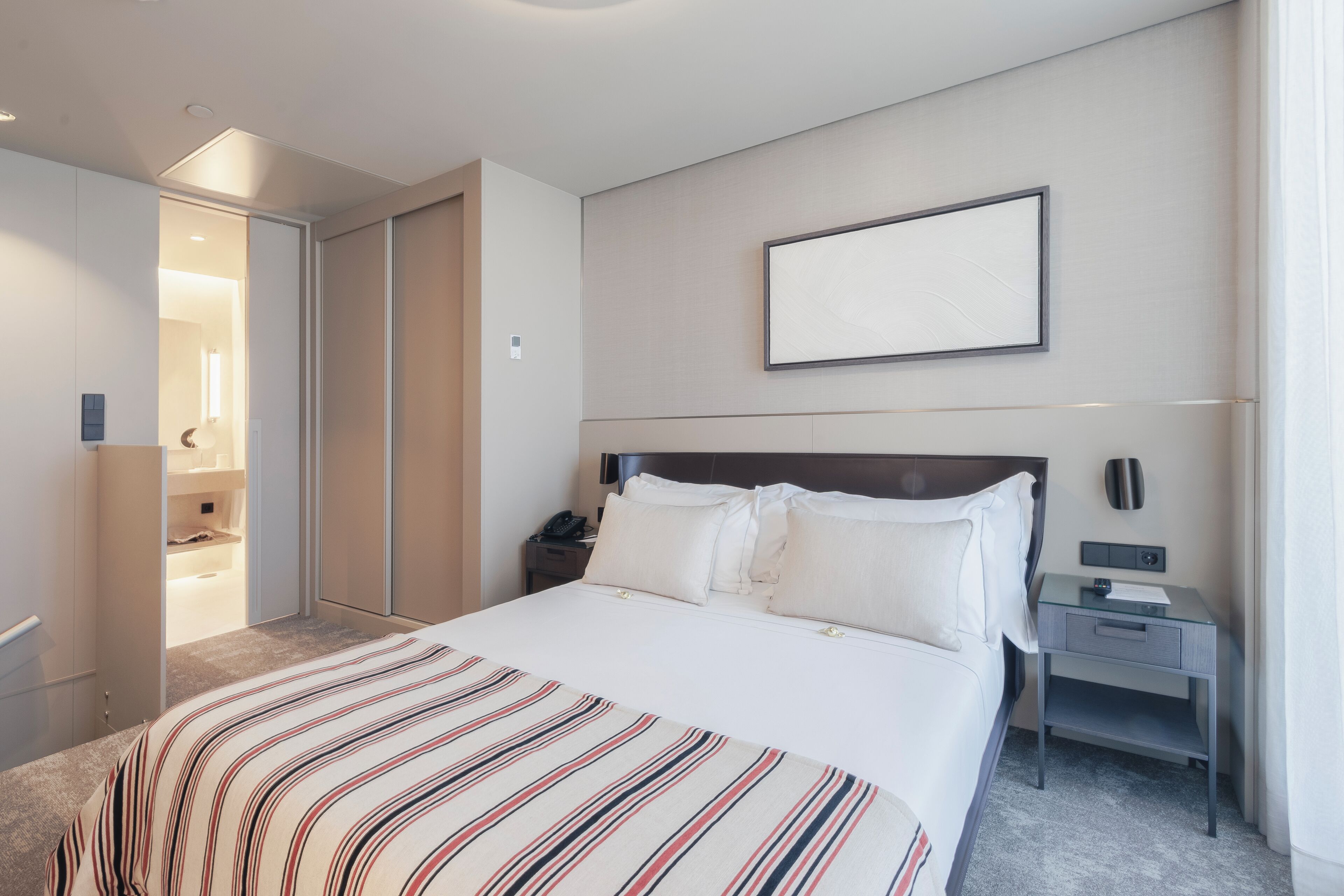 Ein Hotelzimmer mit einem großen Bett, einem Nachttisch, einem Kleiderschrank und einem gerahmten Bild an der Wand.