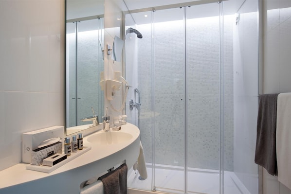 A modern bathroom with a glass-enclosed shower, a large mirror, and a vanity with toiletries. - Hotel White Lisboa (Lisbon)