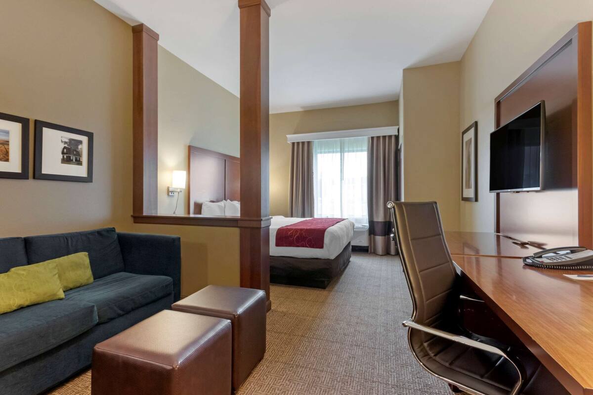 A hotel room with a sofa, a desk, a bed, and a TV.