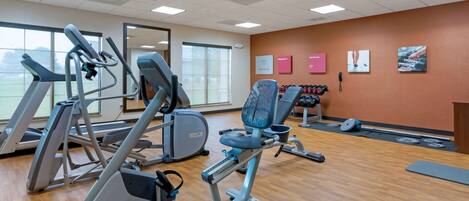 A gym with cardio machines, weightlifting equipment, and a mirror.