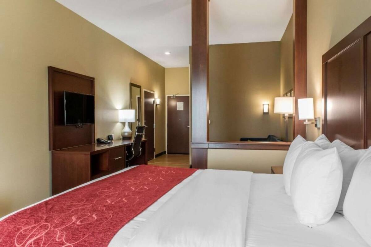 A hotel room with a bed, a desk, a mirror, a television, and a door.