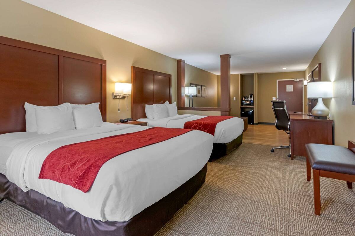 A hotel room with two beds, a desk, a chair, and a lamp.