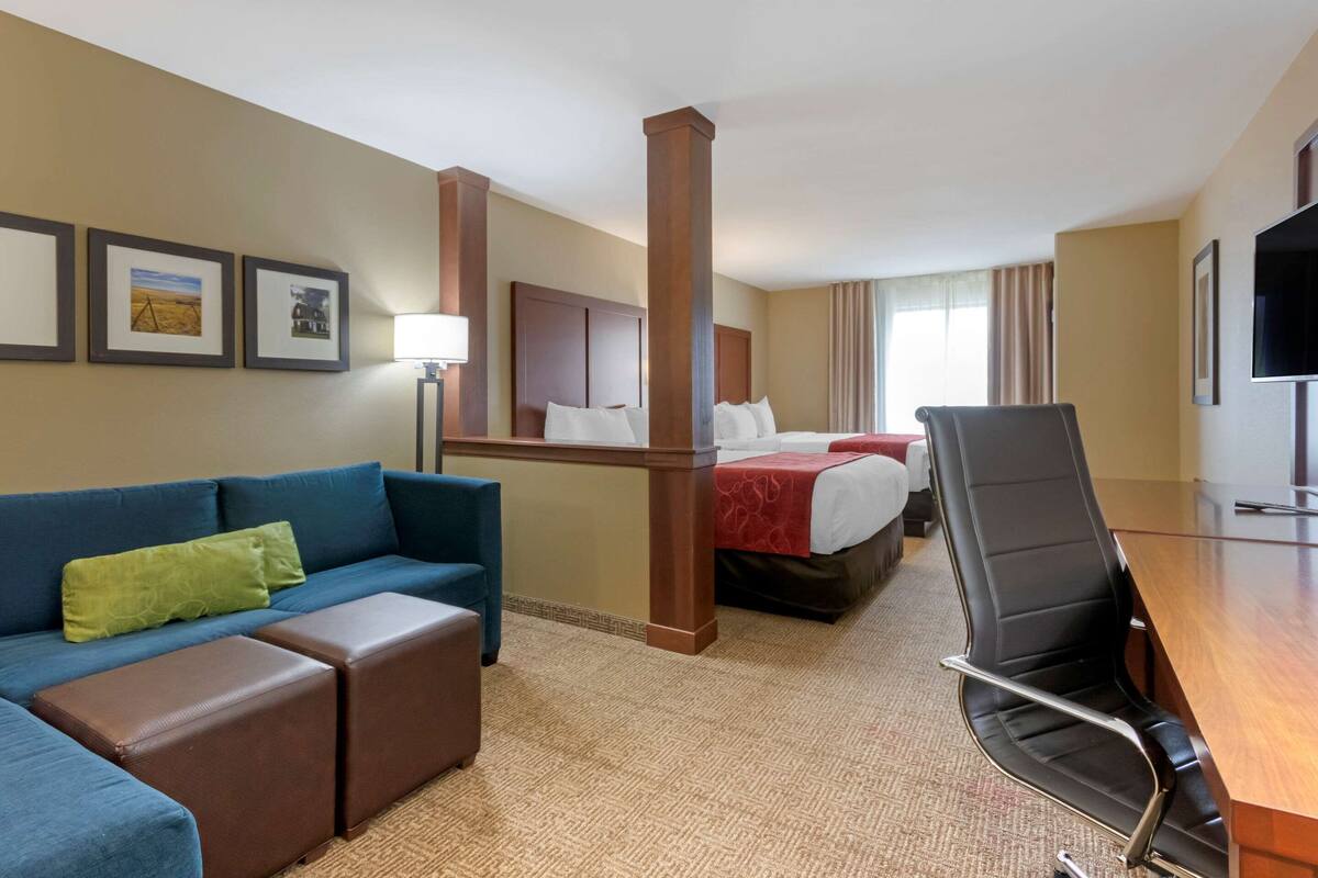A hotel room with a blue sofa, a wooden desk, a bed with a red blanket, and a television on the wall.