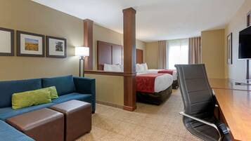 A hotel room with a blue sofa, a wooden desk, a bed with a red blanket, and a television on the wall.