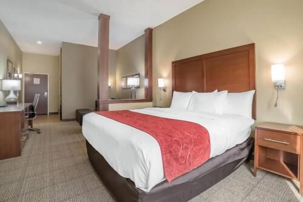 A hotel room with a large bed, a desk, a chair, a nightstand, and a mirror.