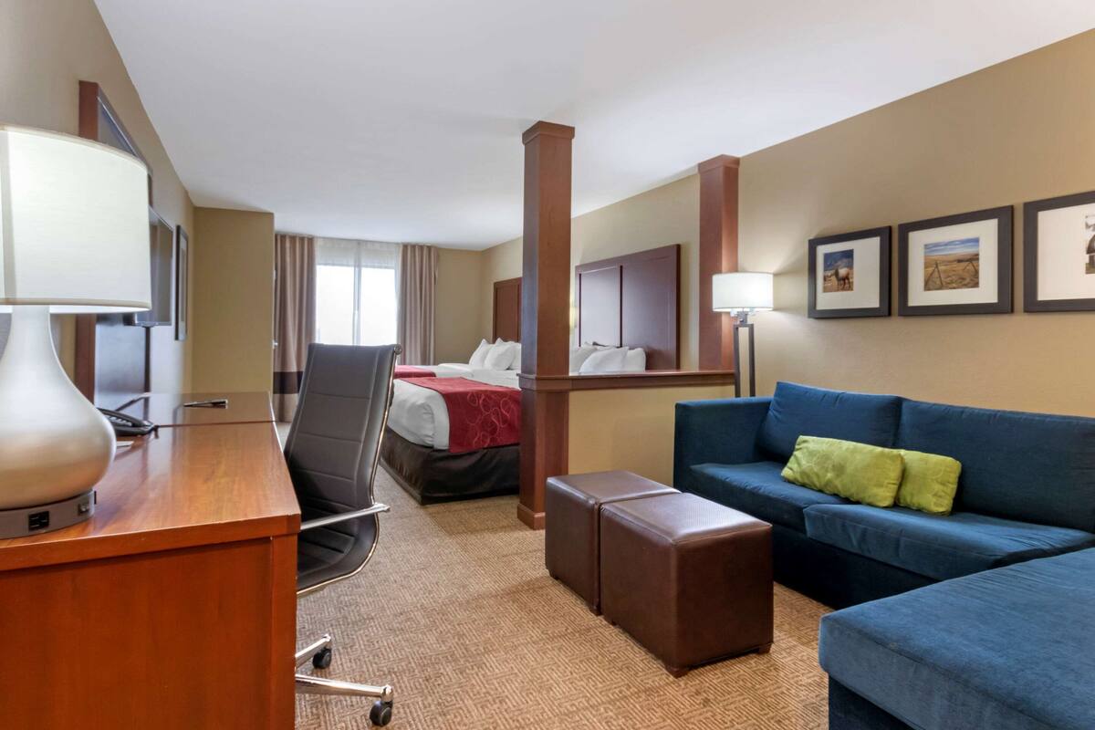 A hotel room with a desk, chair, blue sofa, and a bed with a red blanket.