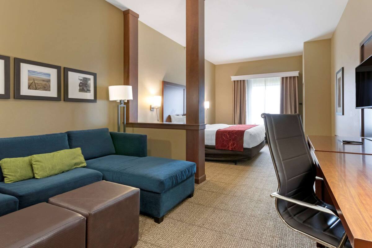 A hotel room with a blue sofa, a wooden desk, a black chair, a bed with a red blanket, and framed pictures on the wall.