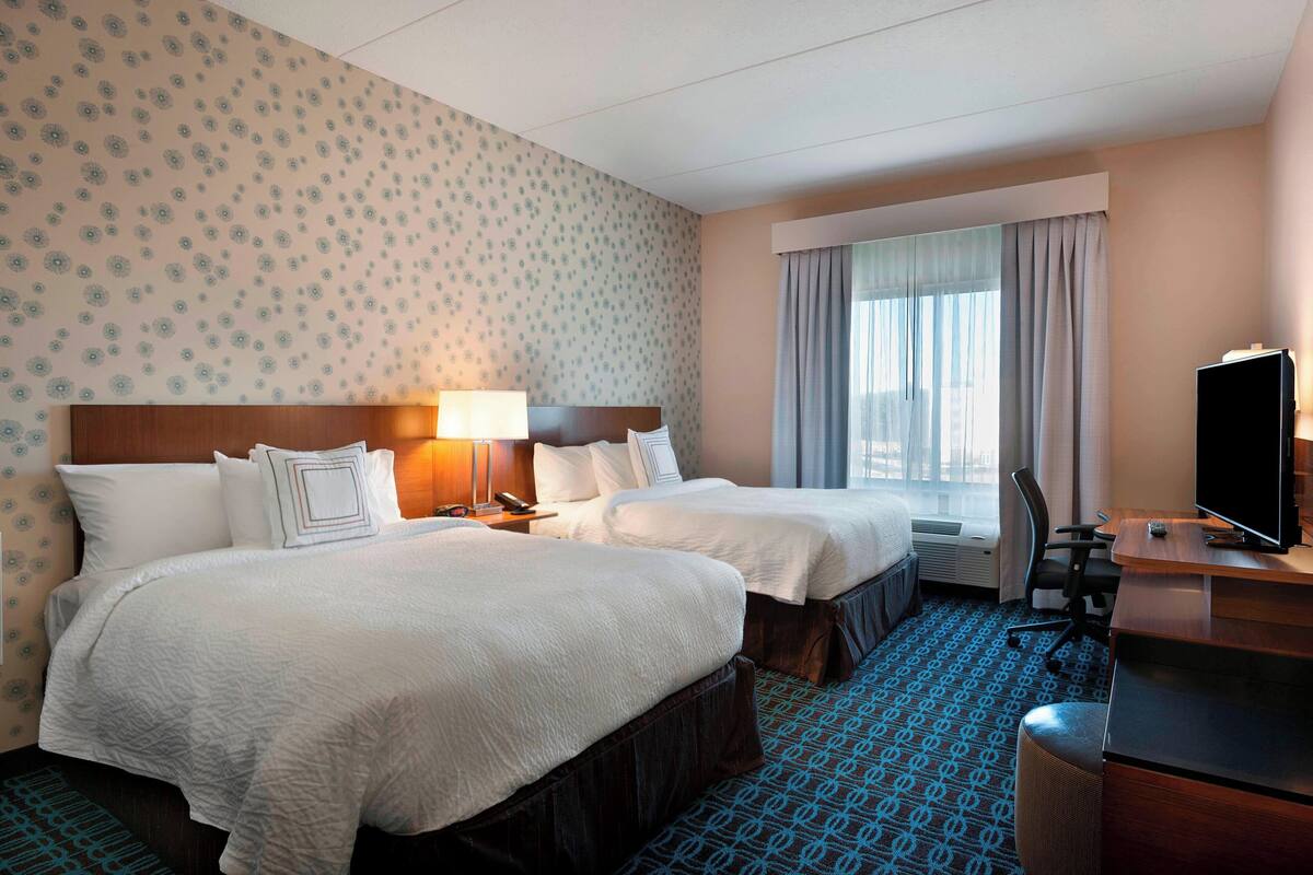 Een hotelkamer met twee bedden, een bureau met een televisie, een stoel en een raam met gordijnen.