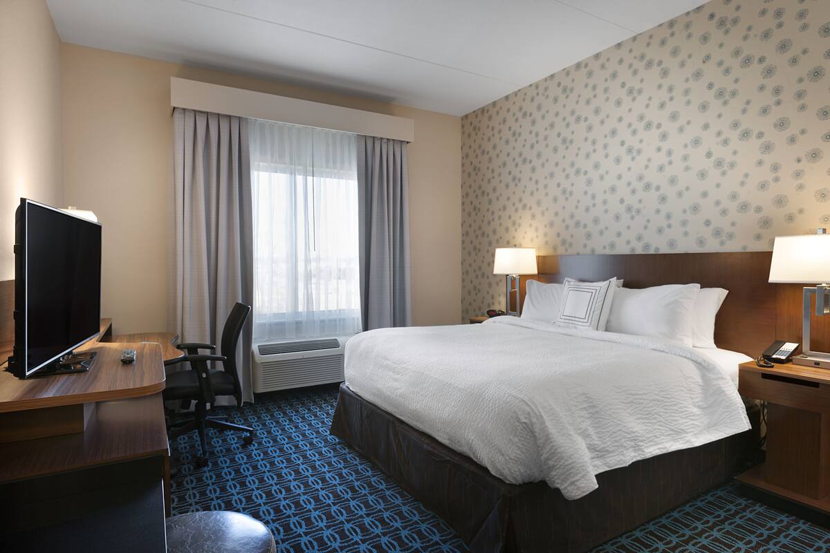 Hotelkamer met een bed, bureau met televisie, stoel, raam met gordijnen en een behang met patroon.