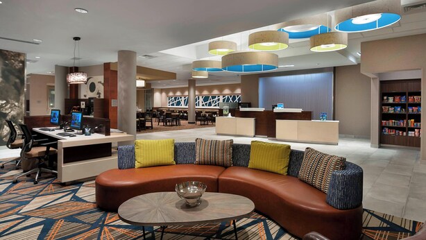 A modern lobby with a curved seating area, a reception desk, and a food service area.