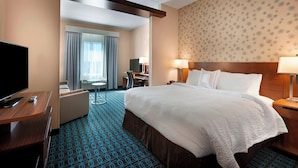 A hotel room with a large bed, a desk, a television, and a seating area.