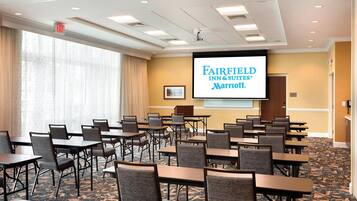 A conference room with tables and chairs, a screen displaying the Fairfield Inn & Suites Marriott logo, and a carpeted floor.