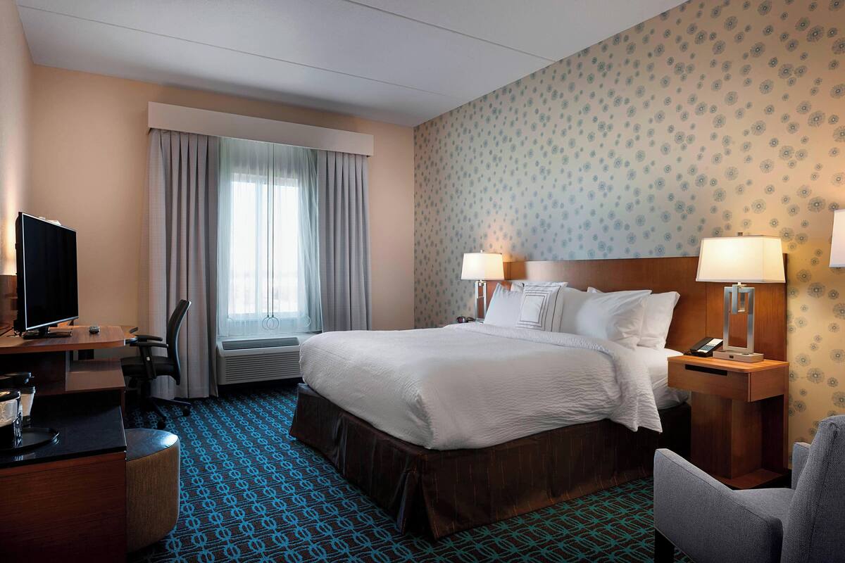 Een hotelkamer met een groot bed, twee bedlampen, een bureau met een televisie en een stoel.