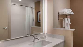 Un baño moderno con un espejo grande, un lavamanos, una cortina de ducha y un perchero con toallas dobladas.