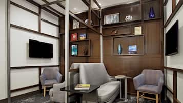 Una habitación de hotel moderna con una televisión de pantalla plana, dos sillones, un sofá, una mesita y una estantería con objetos decorativos.