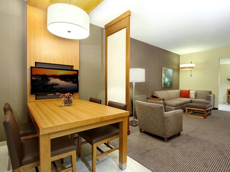 Una habitación de hotel con una mesa de comedor de madera, sillas de cuero marrón, un sofá y un televisor montado en la pared.