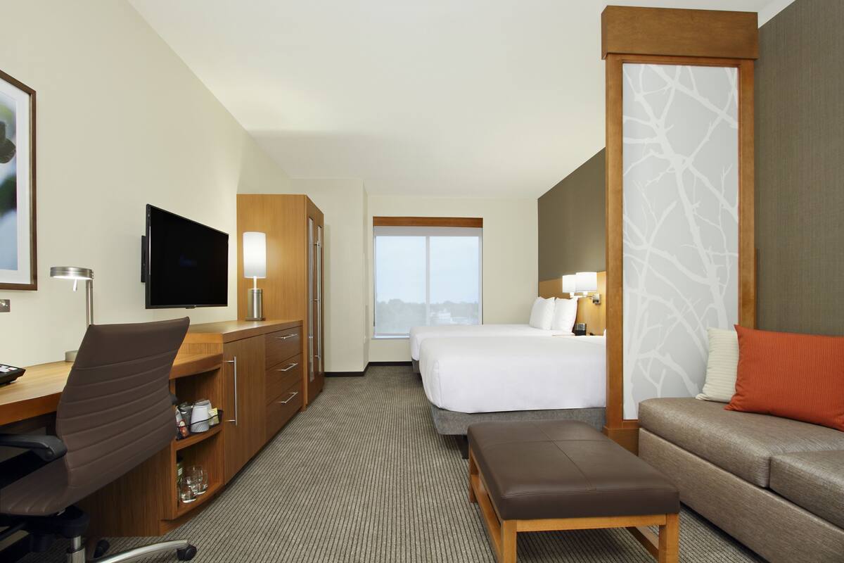 Ein Hotelzimmer mit Schreibtisch, Stuhl, Fernseher, Bett und Schlafsofa.