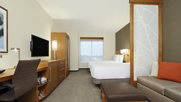 A hotel room with a desk, chair, TV, bed, and sofa.