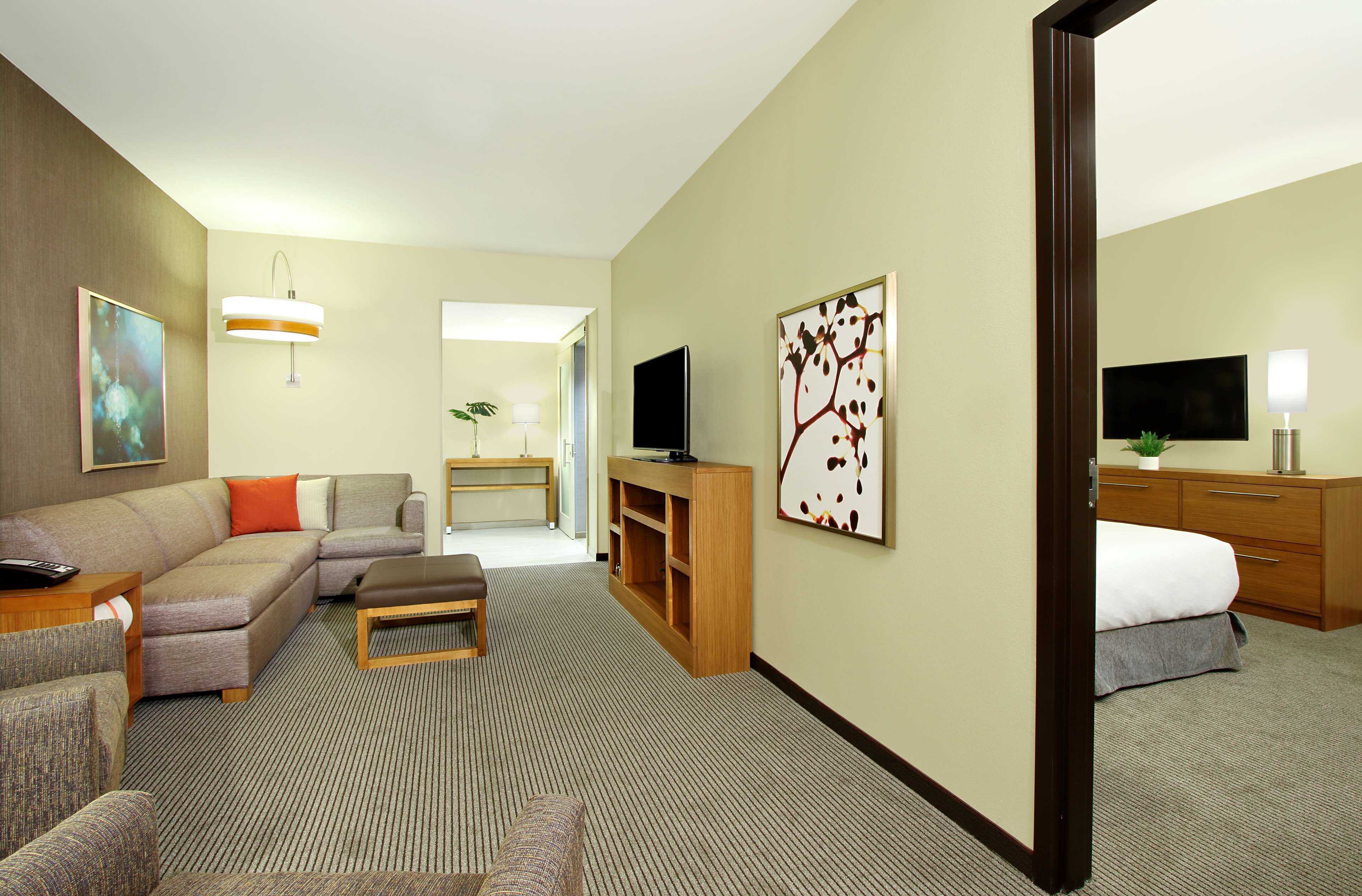 A hotel room with a sectional sofa, a small table, a TV, a desk, and a bed.