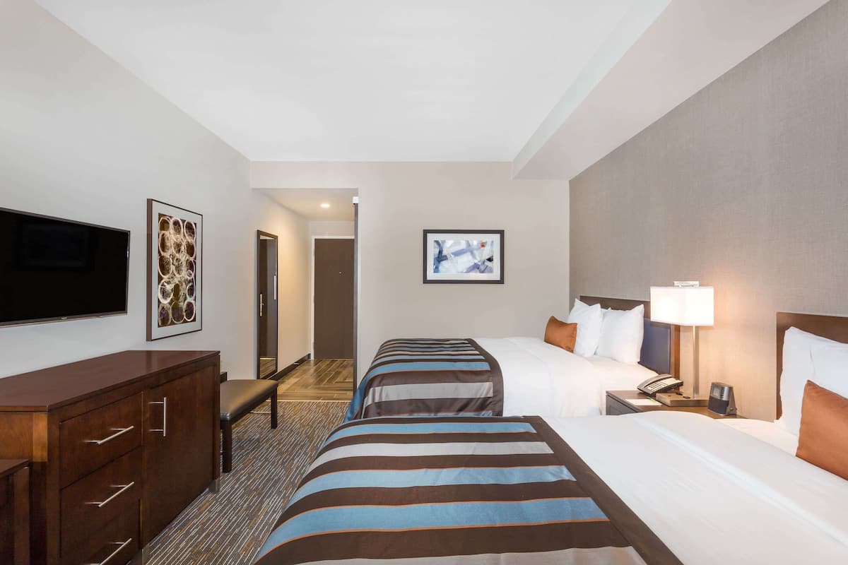 A hotel room with two beds, a desk, a TV, and artwork on the walls.