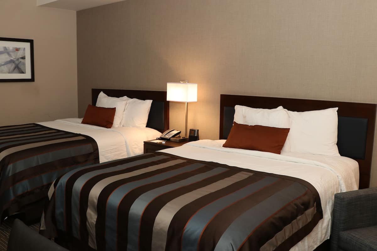 A hotel room with two beds, each with striped bedding, a nightstand with a lamp, and a framed picture on the wall.