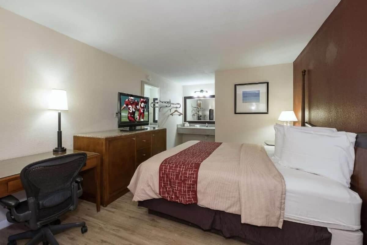 A hotel room with a bed, desk, chair, TV, and a mirror.