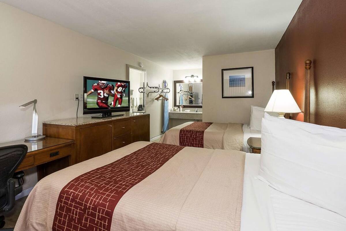 A hotel room with two beds, a TV, a desk, and a mirror.