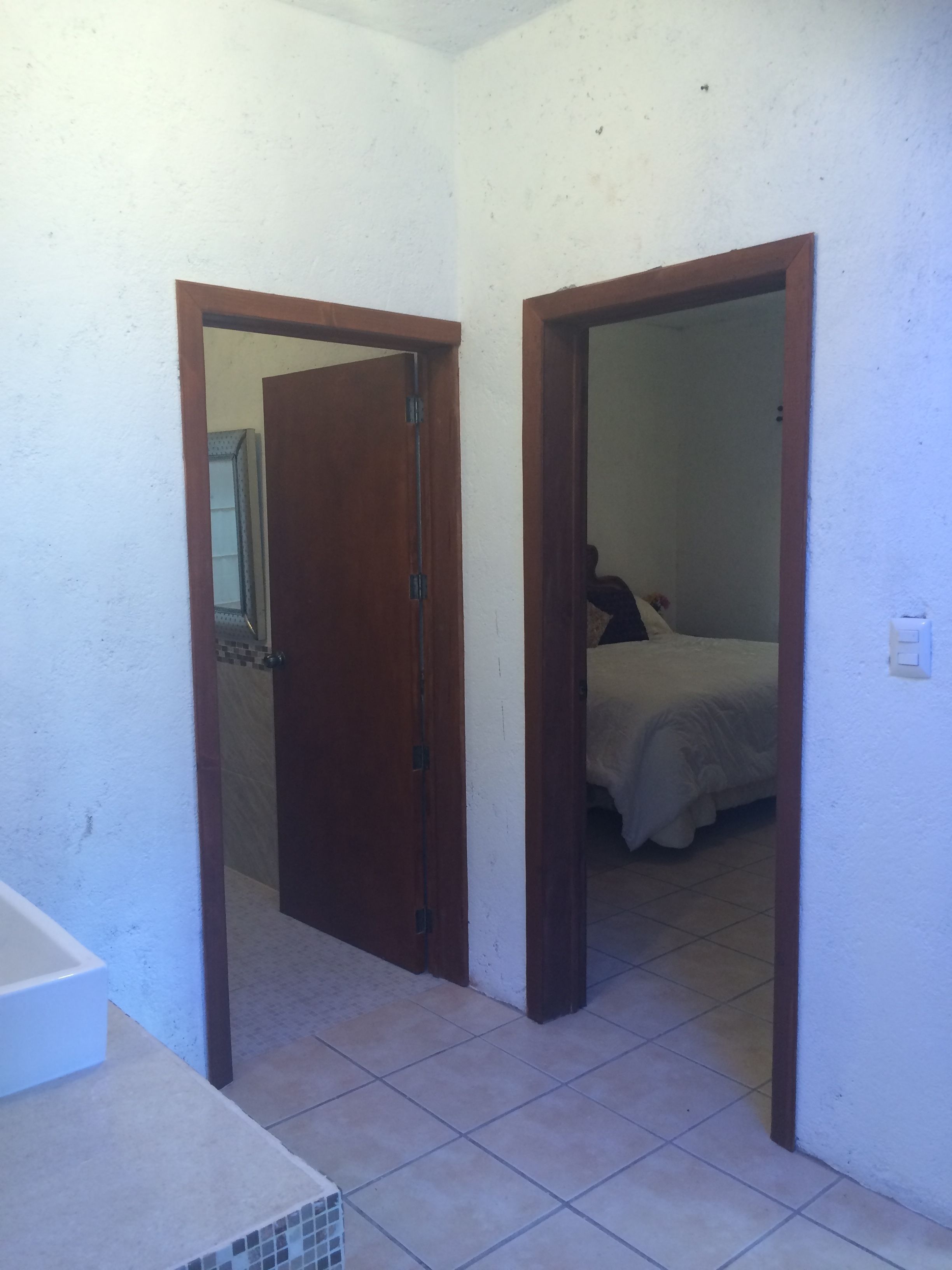A room with a bed, a bathroom with a sink, and a door leading to another room.