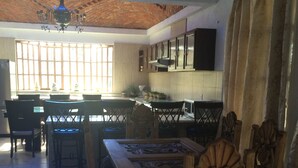 A dining area with a wooden table and chairs, a chandelier, and a kitchen in the background. - Casa de la Montaña (San Miguel de Allende)