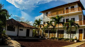 A two-story building with a balcony, surrounded by palm trees and a clear sky. - Hotel Popoyo (Tola)