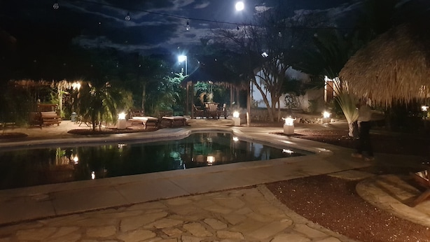 A nighttime pool area with a clear view of the pool, surrounding lounge chairs, and a thatched-roof structure. - Hotel Popoyo (Tola)