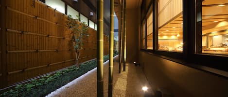 A corridor with a bamboo fence, pebbles, and a view of a restaurant area.