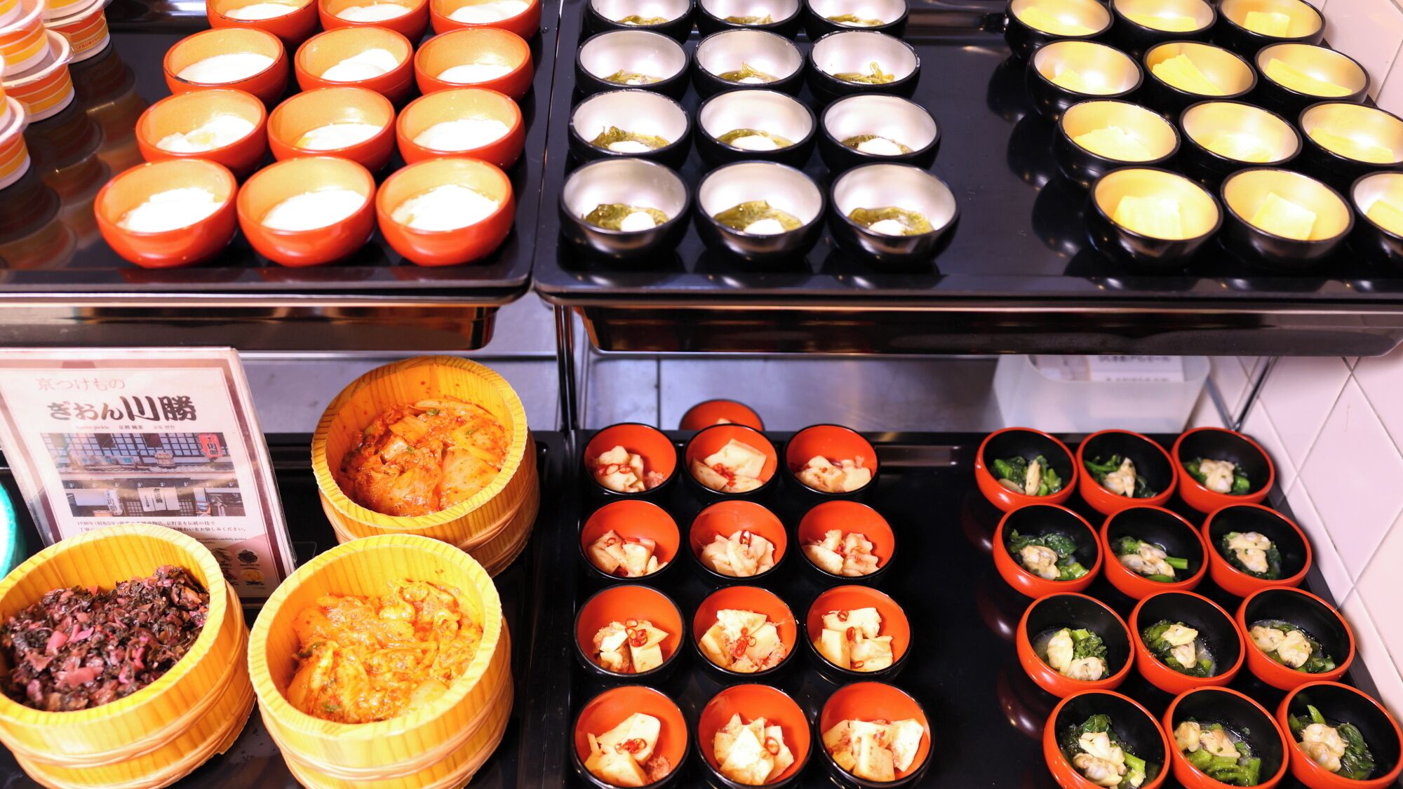 A variety of food items displayed in different colored bowls and containers, likely in a restaurant or food market setting.