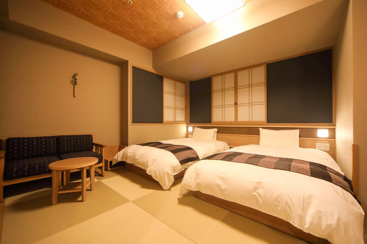 A hotel room with two beds, a sofa, and a small table.