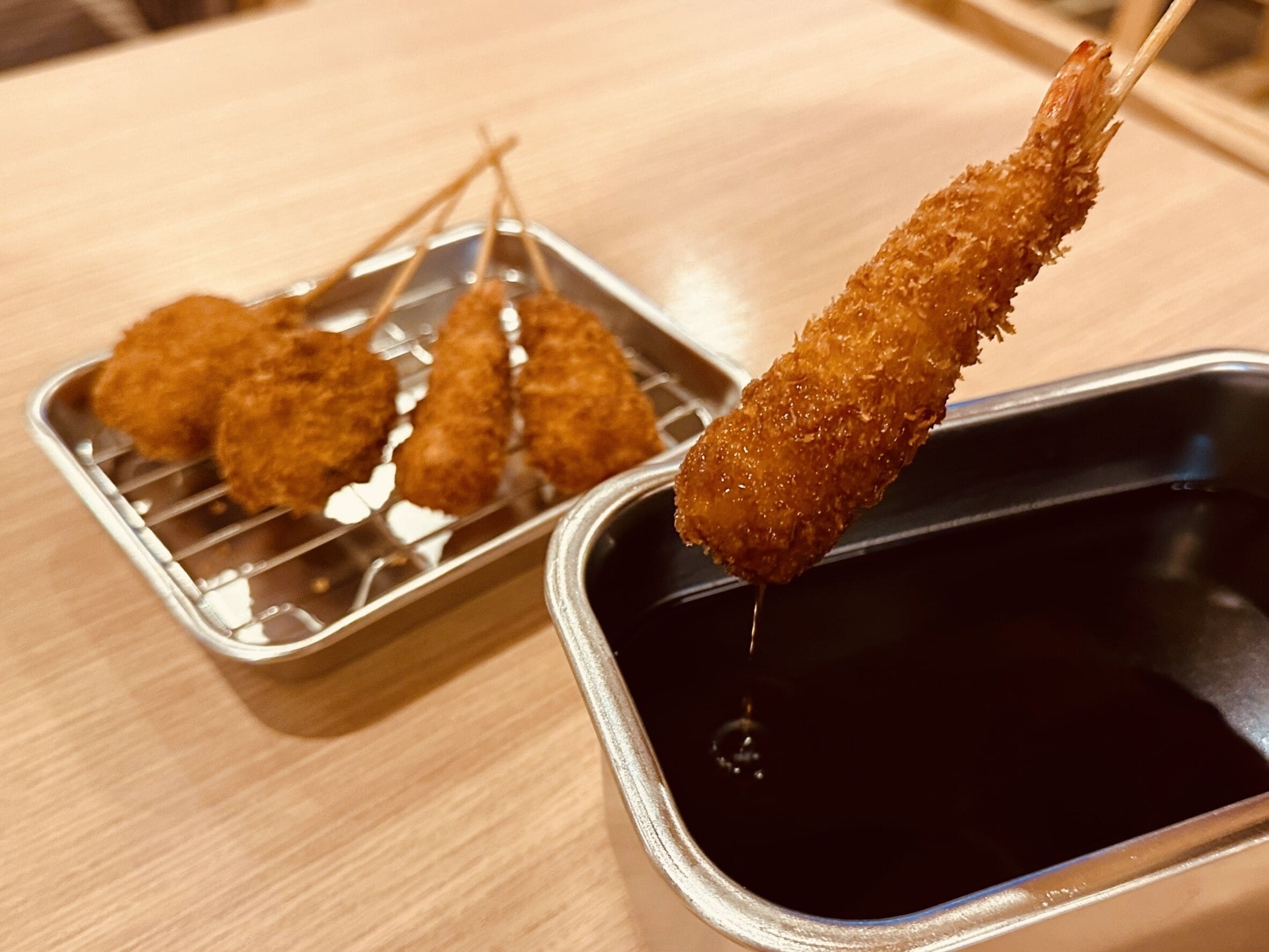 A tray of breaded and fried food items, possibly croquettes, with a dipping sauce in a metal container.