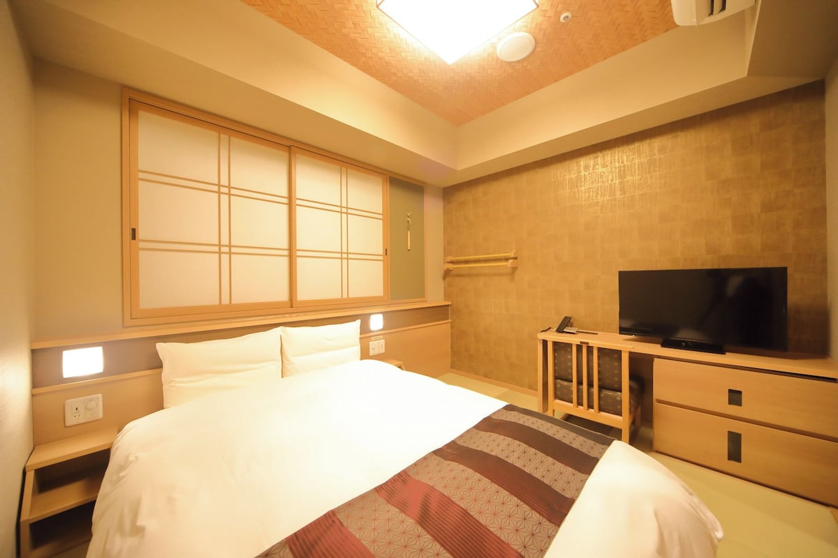 A hotel room with a bed, a television, a desk, and a cabinet.