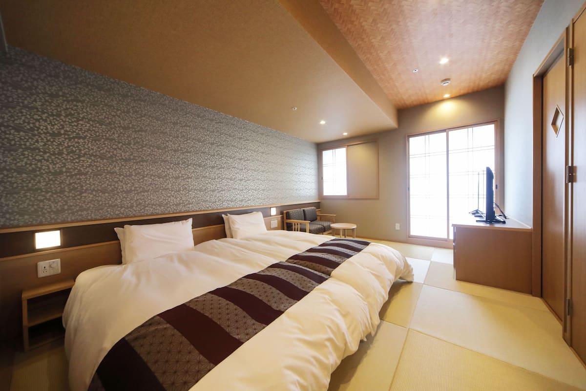 A hotel room with a large bed, a small desk, a chair, a TV, and a window with a view.