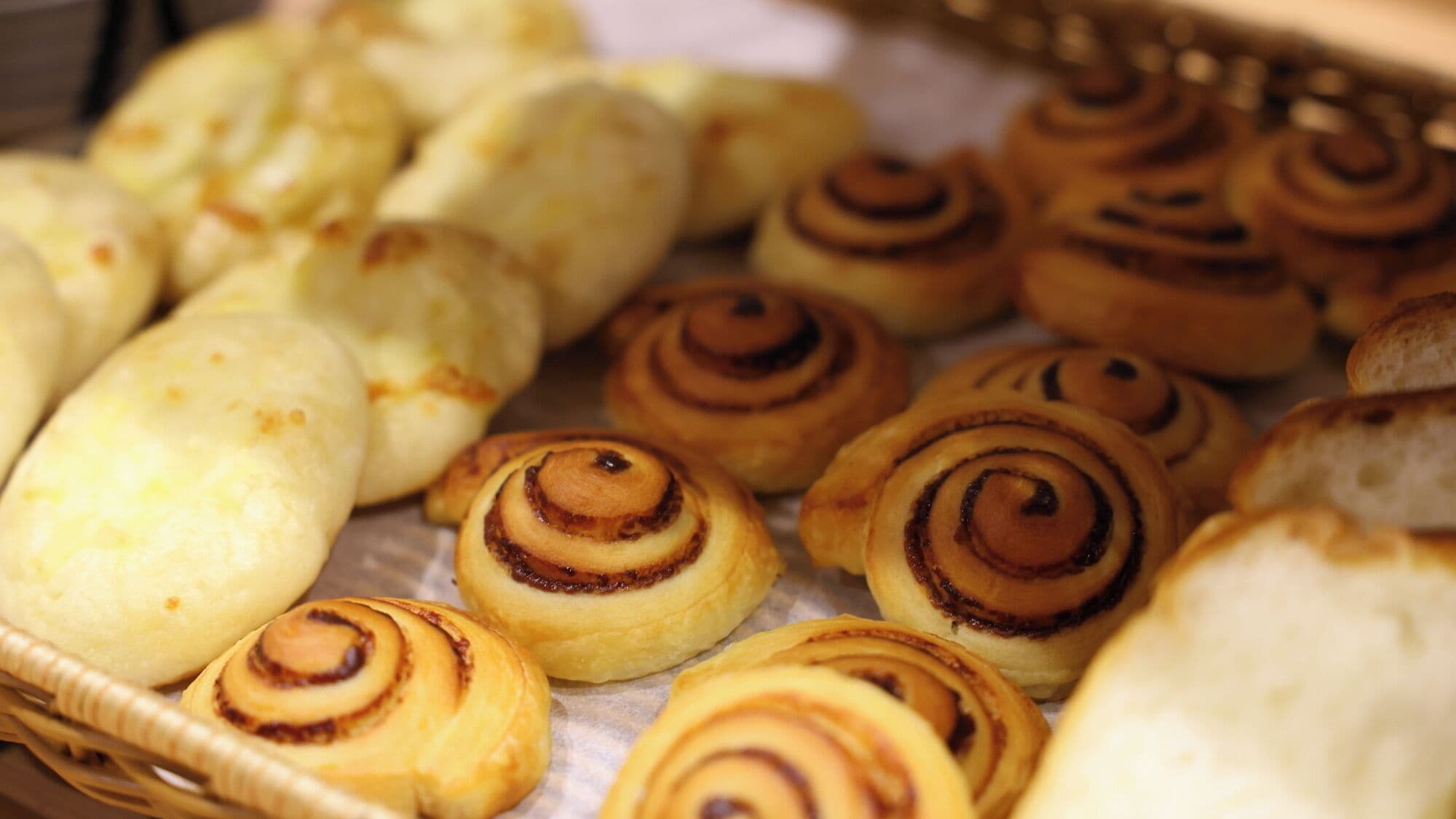 A variety of baked goods, including cinnamon rolls and other pastries, displayed in a basket.