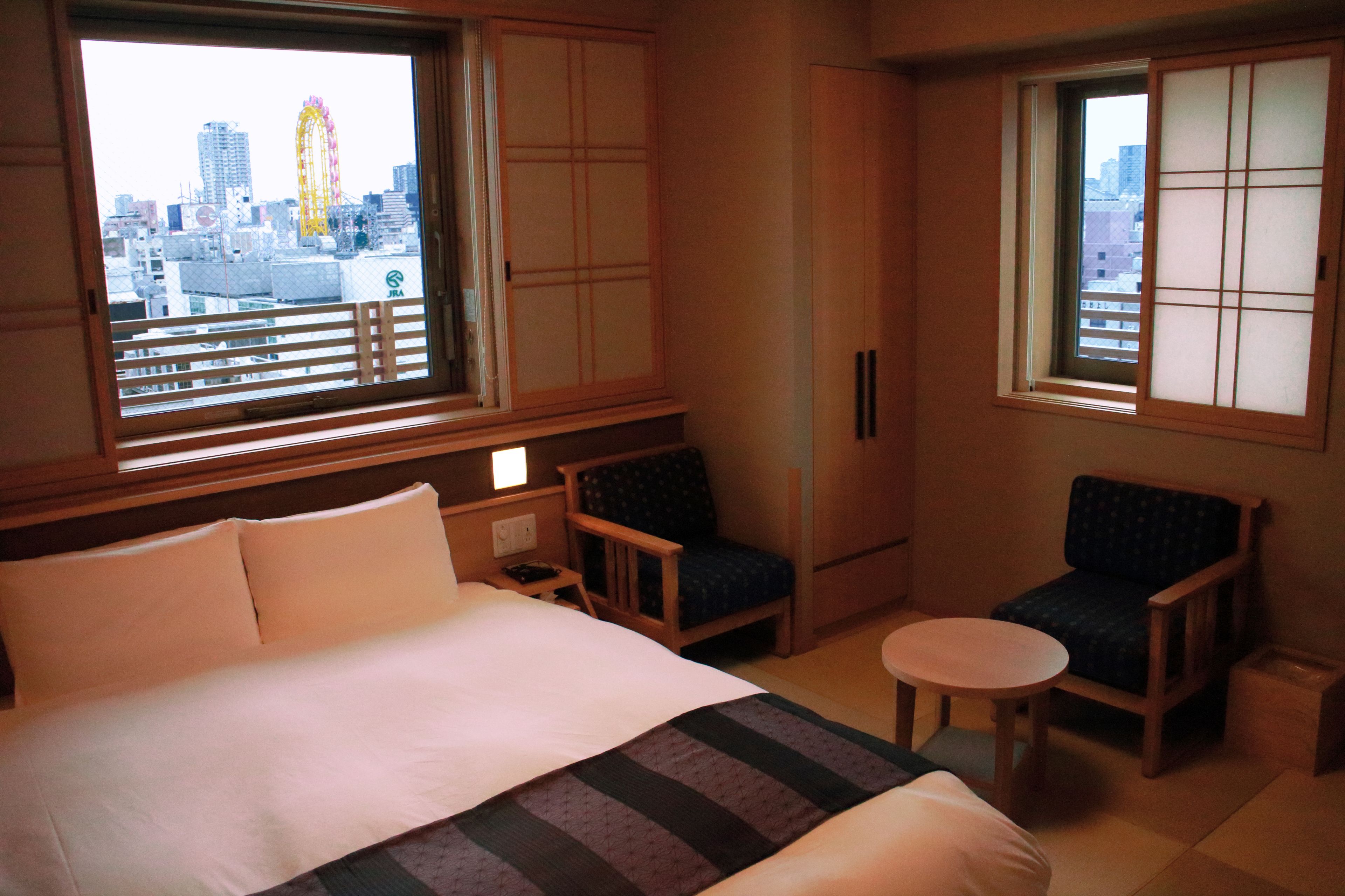 Una habitación de hotel con cama, dos sillas, una mesita y ventana con vista a la ciudad.