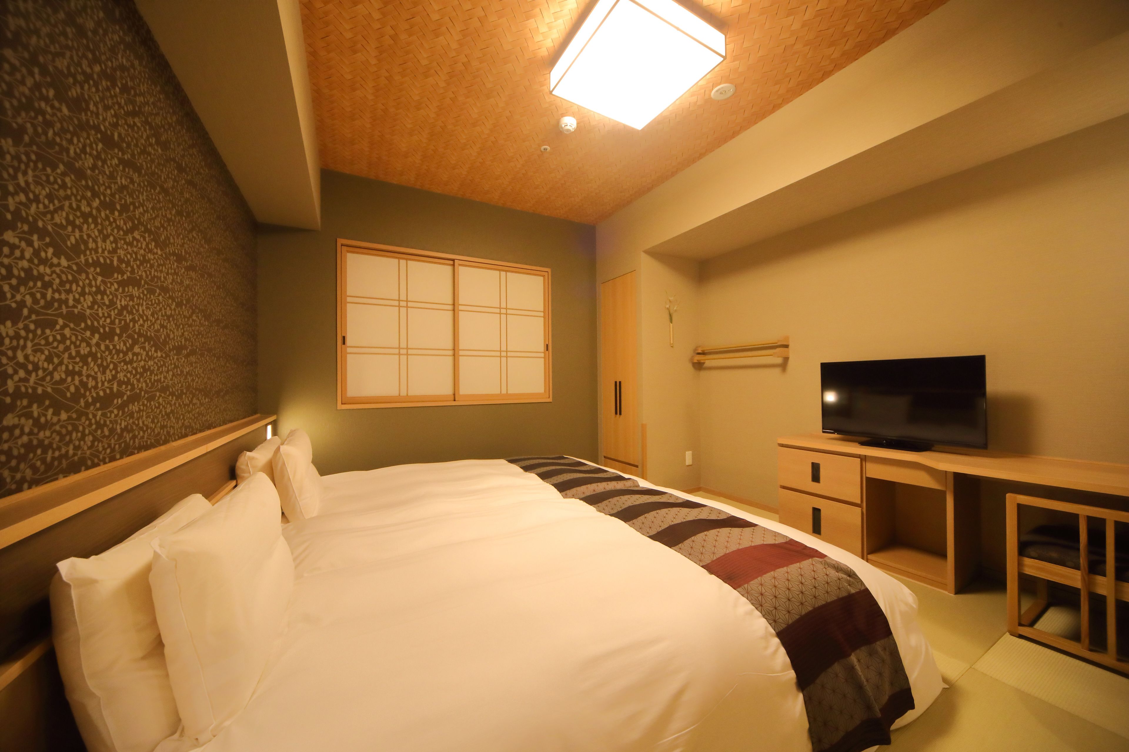 Quarto de hotel com uma cama, televisão, escrivaninha de madeira e uma porta deslizante japonesa tradicional.