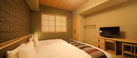 Quarto de hotel com uma cama, televisão, escrivaninha de madeira e uma porta deslizante japonesa tradicional.