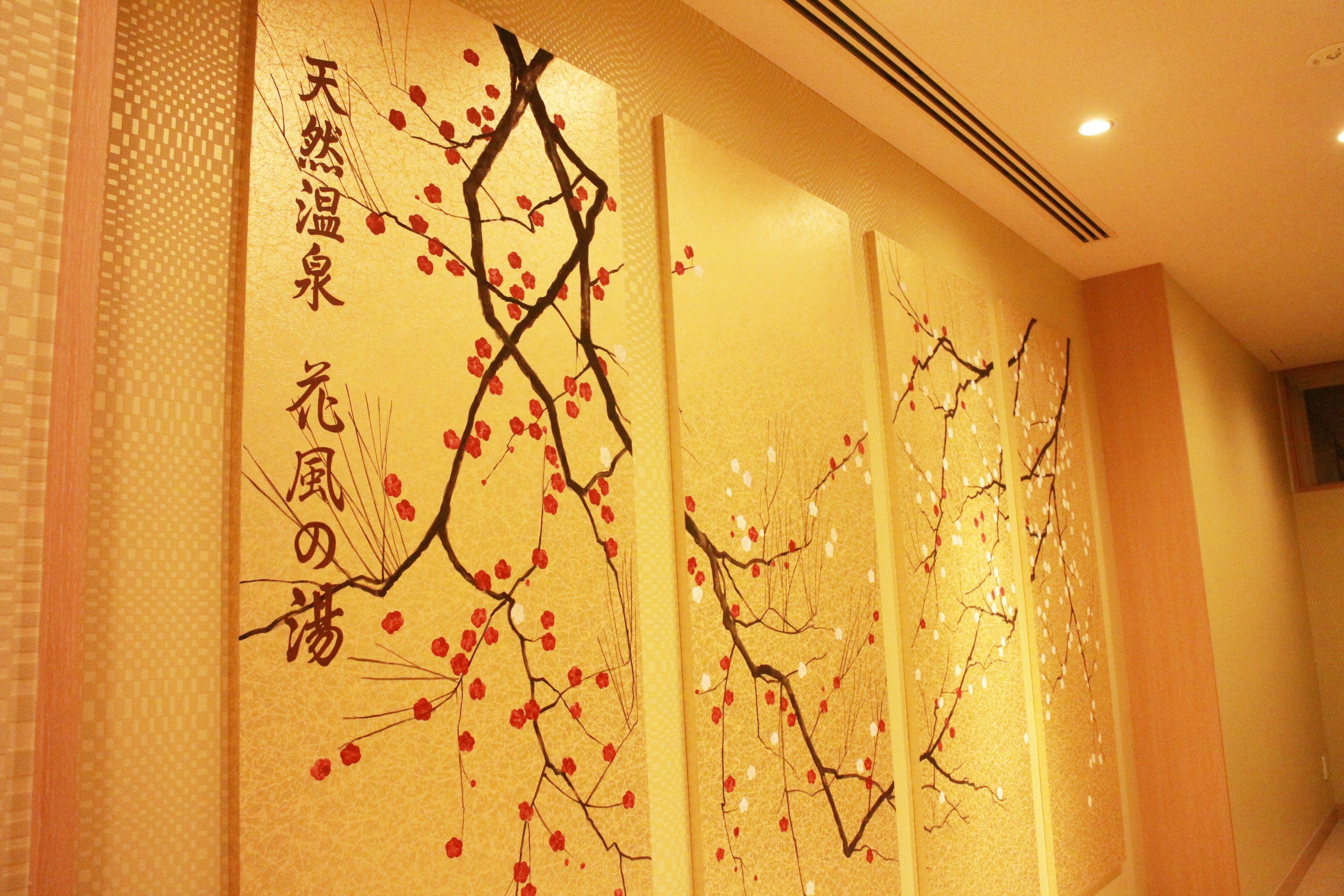 Een muur met een decoratief paneel waarop takken met rode en witte bloemen en Japanse kalligrafie afgebeeld zijn.