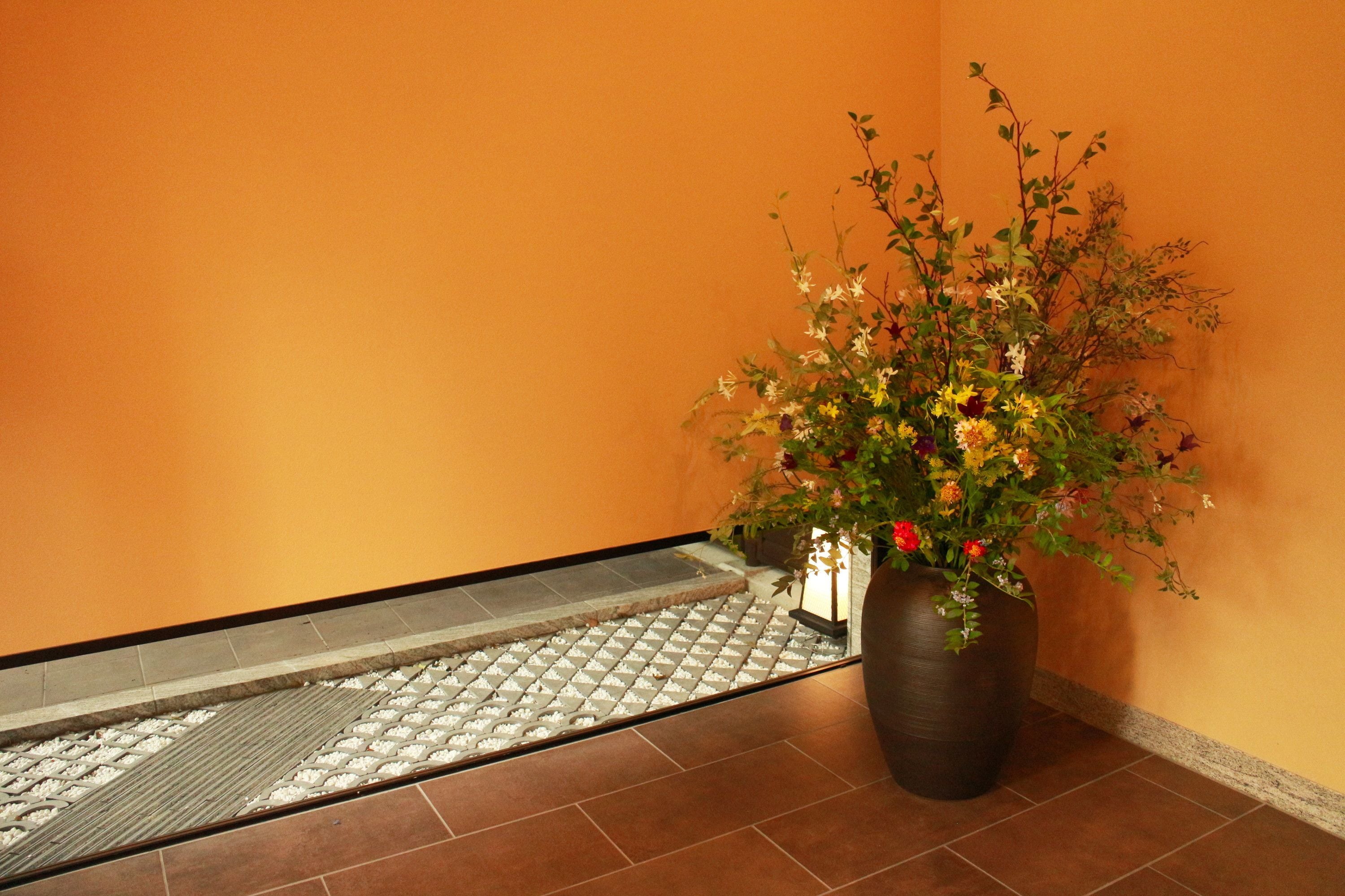 A hallway with a tiled floor, a potted plant with flowers, and a small table with a lamp.