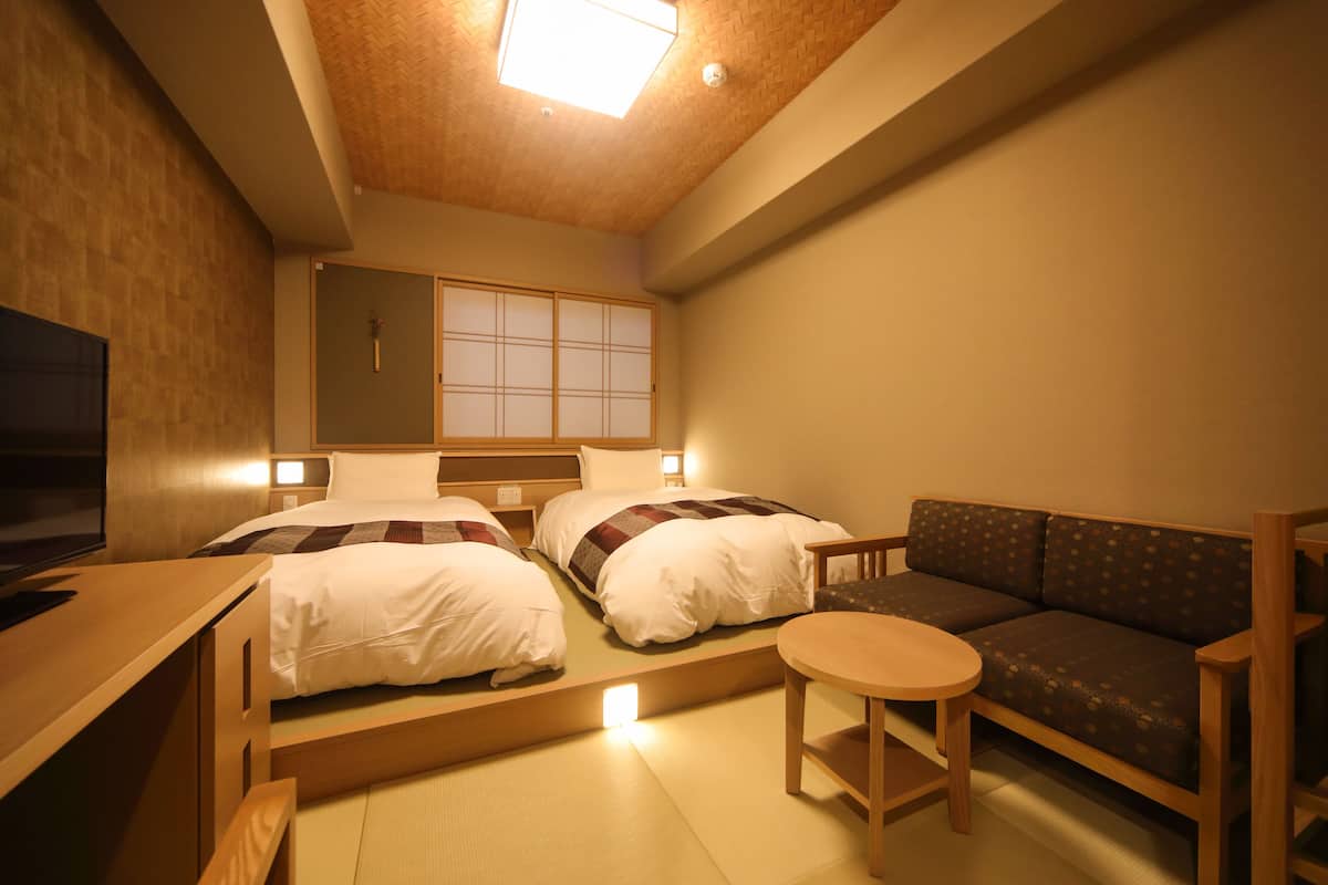 A hotel room with two beds, a sofa, a small table, and a TV.